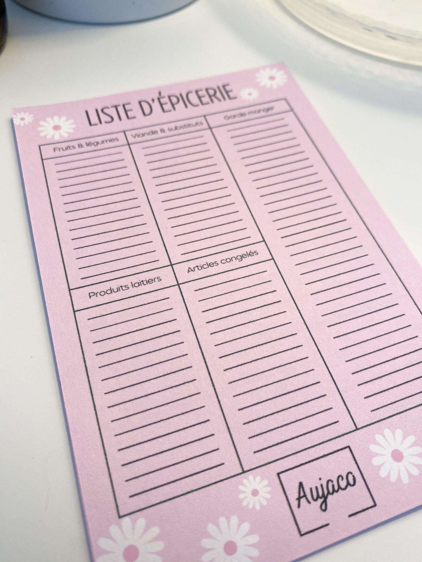 alt="Liste d'épicerie au format 4x6 pouces, design simple sur fond rose avec marguerites blanches, sections pour fruits et légumes, viande et substituts, garde-manger, produits laitiers et articles congelés, plusieurs lignes spacieuses, 40 pages, papier cartonné épais pour une durabilité supérieure."