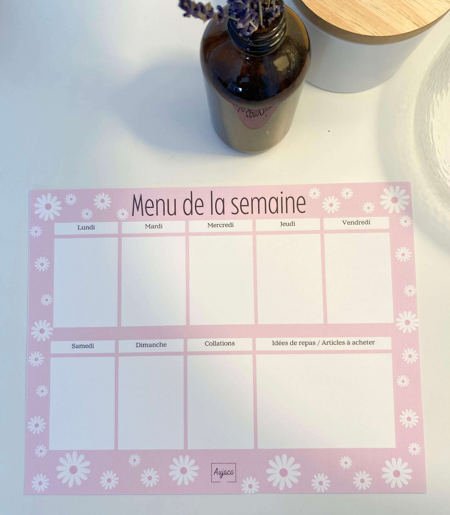 alt="Planificateur de repas hebdomadaire Pink Era avec des marguerites blanches, design simple et féminin de couleur rose, sections dédiées pour chaque jour et collations, grand espace pour noter idées de repas et articles à acheter, format compact 8.5 x 11 pouces, 40 pages, option aimants, papier cartonné épais pour une durabilité supérieure."