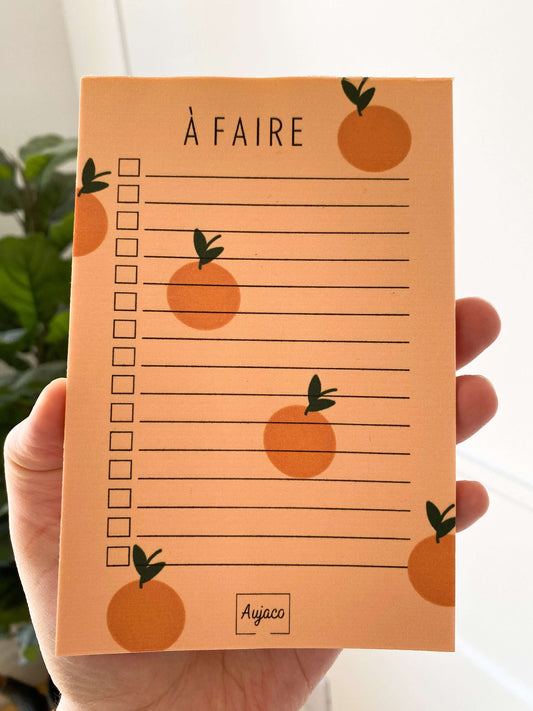alt="To-do list avec design sur fond orange agrémenté de petites oranges, format compact 4 x 6 pouces, plusieurs cases à cocher pour les tâches, papier cartonné épais pour une meilleure durabilité, 40 pages, dessiné et produit par Aujaco."
